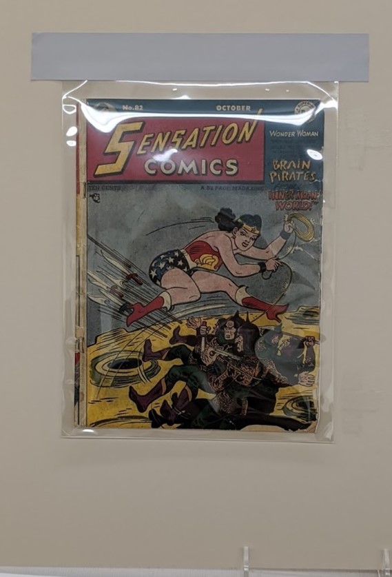 Display for Sensation Comics #82 Comic book featuring Wonder Woman lassoing two other figures, under clear plastic in a mat