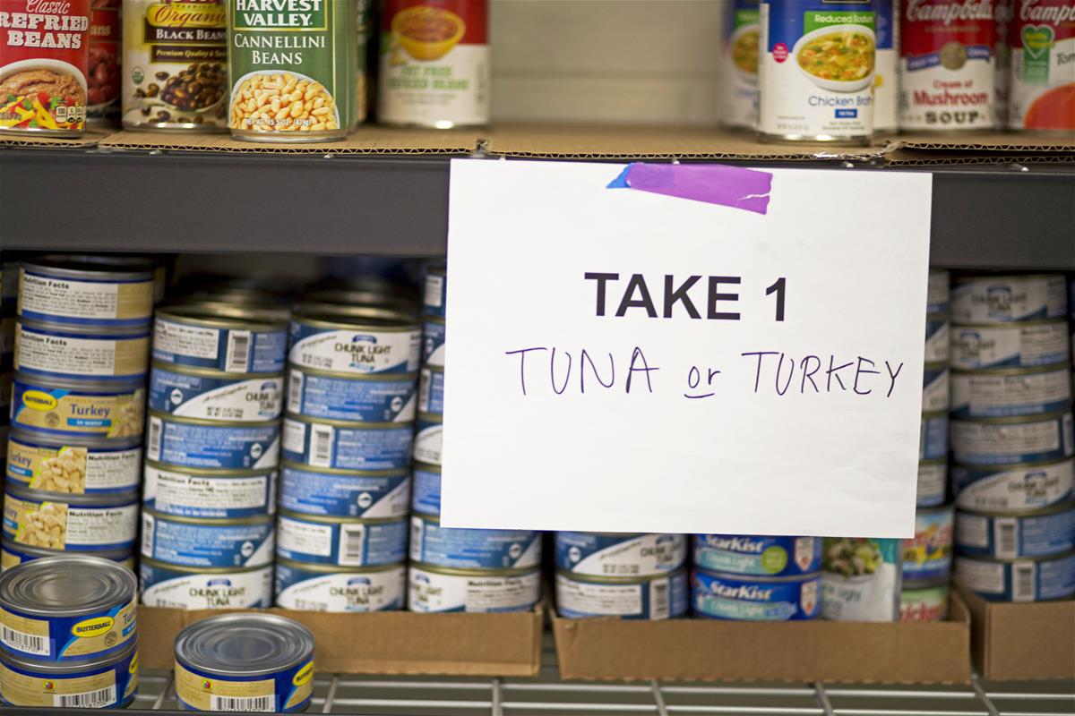 Shelves with cans of tuna, turkey, and vegetables, with sign reading 