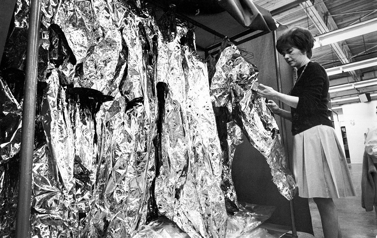 Woman examines a thin mylar suit hanging in a rack of similar suits