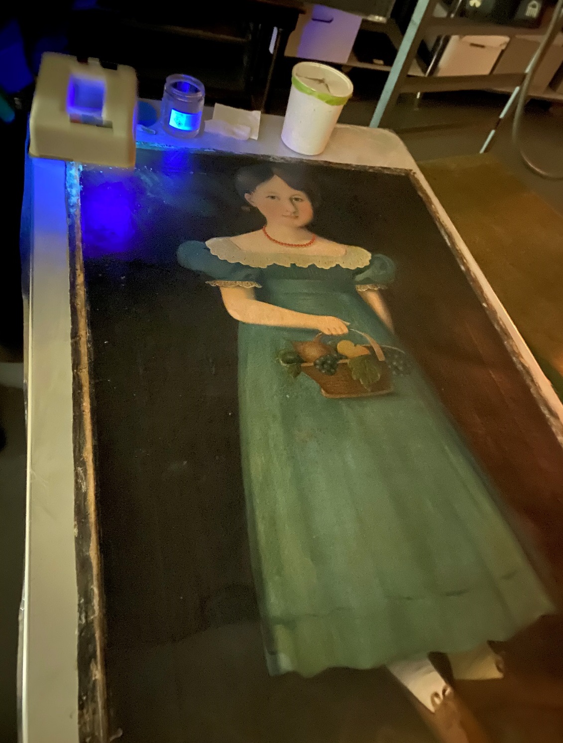 UV light to aid in cleaning Painting of girl in blue dress, laid flat on table with blue light and tools at one end