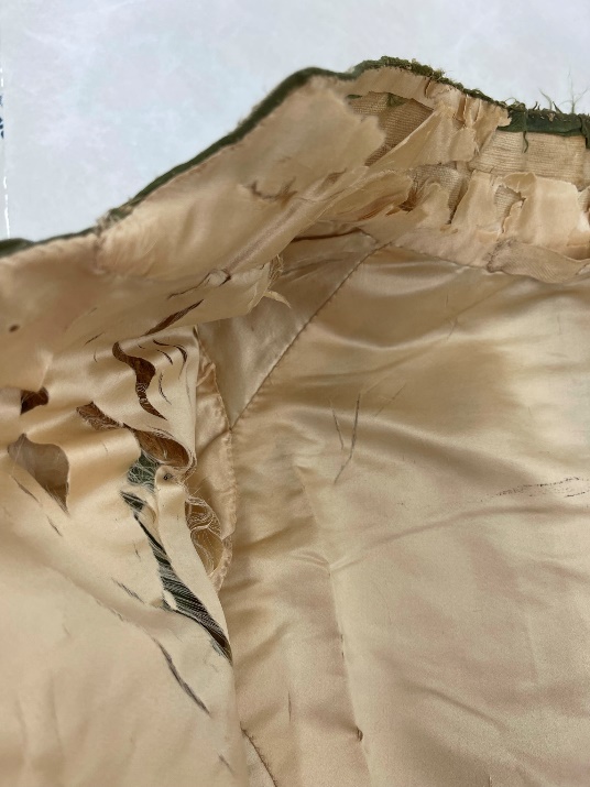Detail of beige silk coat lining with many rips and frayed edges