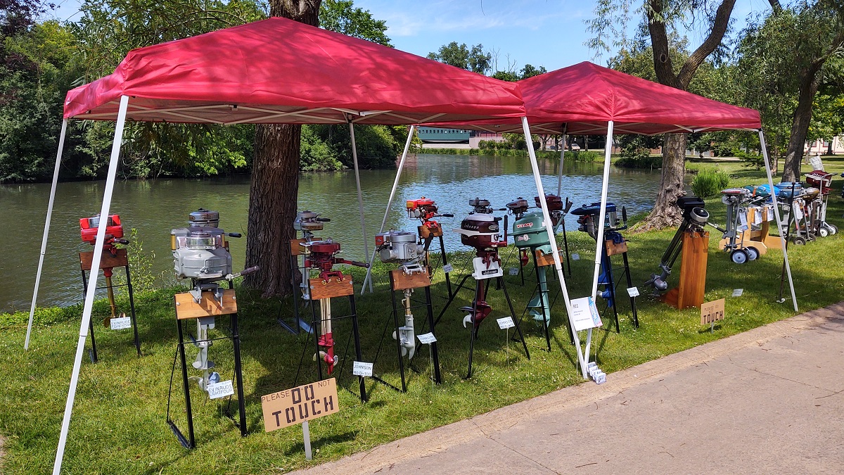 Display of motors on stands under red tents in front of a lake or other body of water