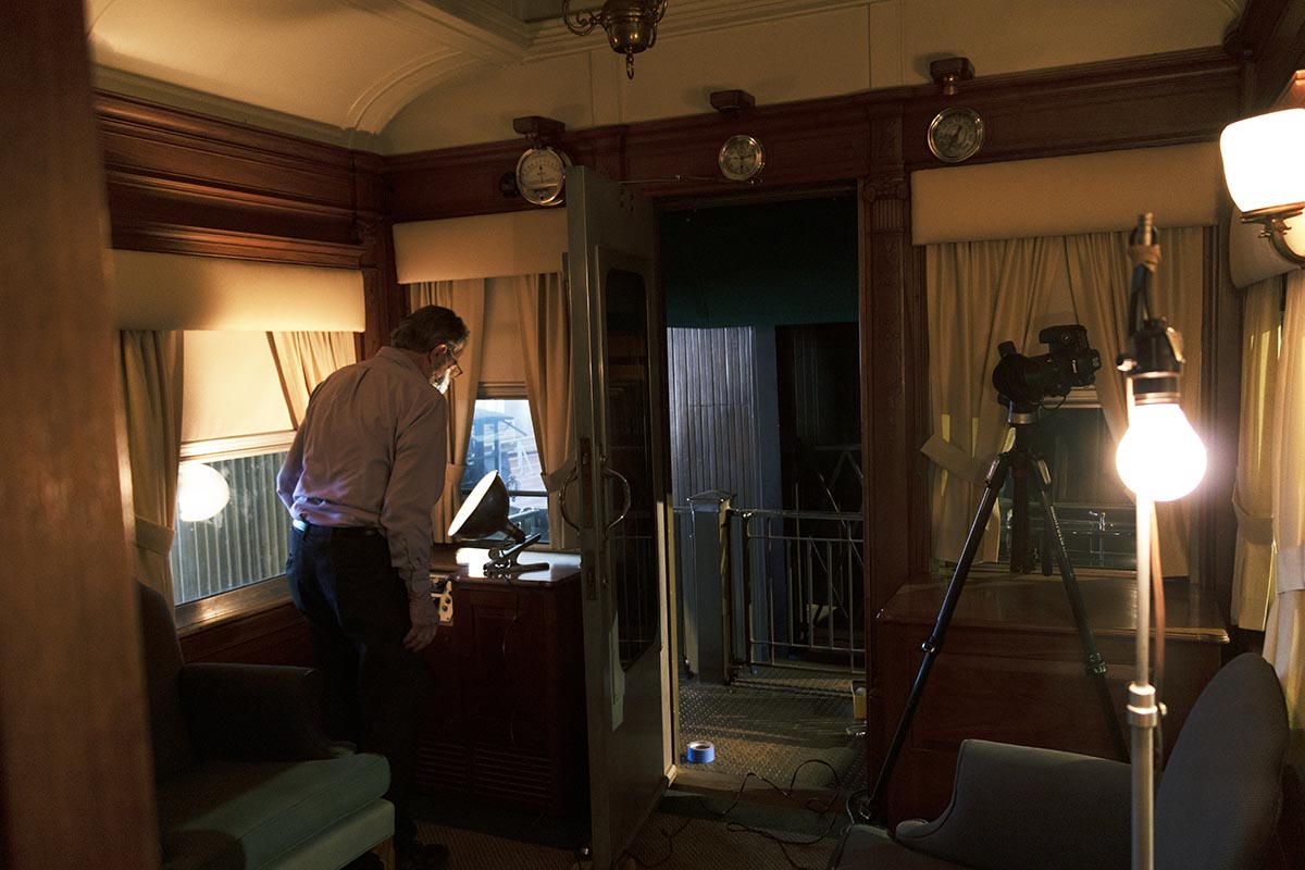 Interior space with coved ceiling, containing a man bending over a light, with other lights and a camera on a tripod in the space