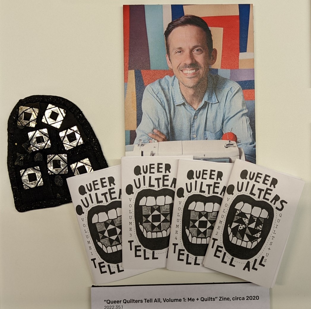 Photo of Zak Foster, his “mini-quilt,” and co-authored “zines Photo of man, arch-shaped fabric with shiny silver squares, and four booklets with graphic of mouth with teeth and text