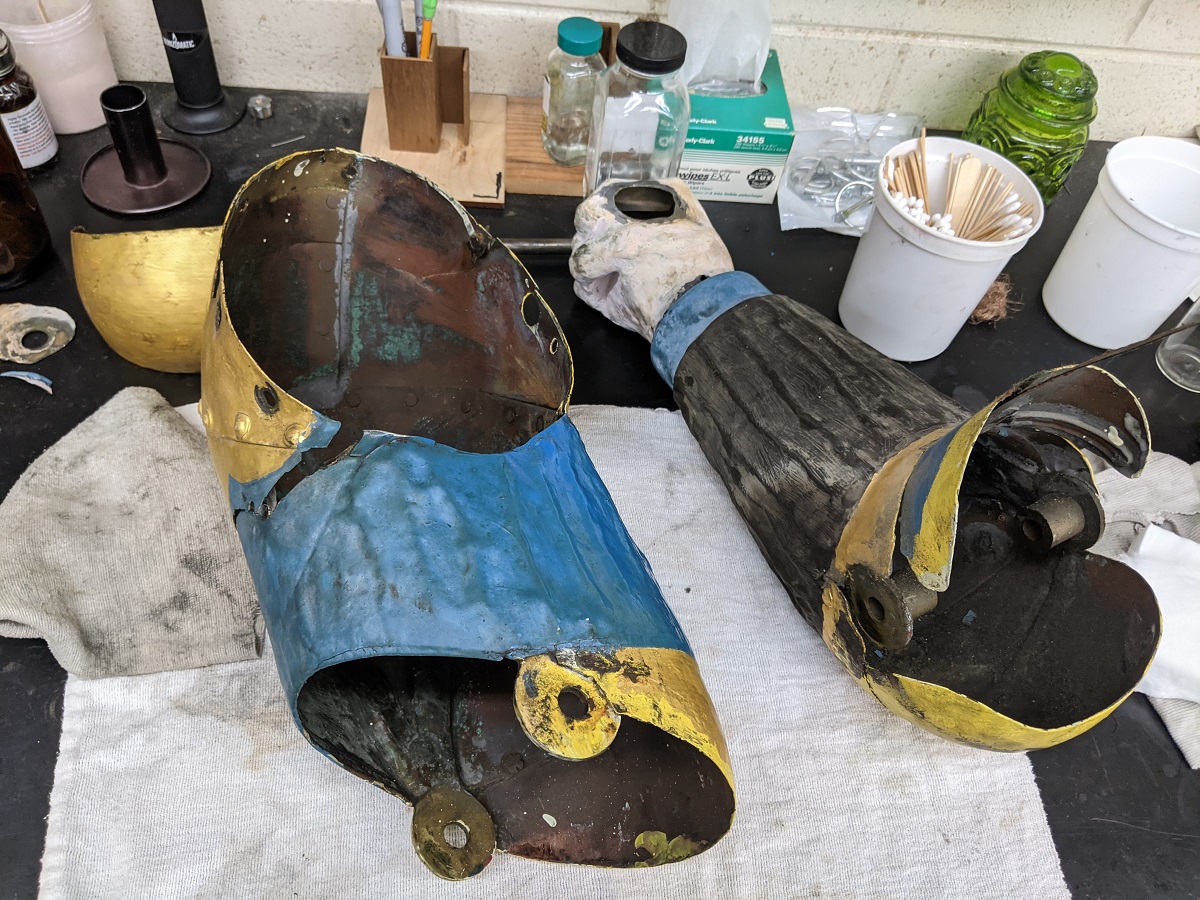 Painted metal pieces, one in the shape of a forearm and hand, on a cloth on a workbench