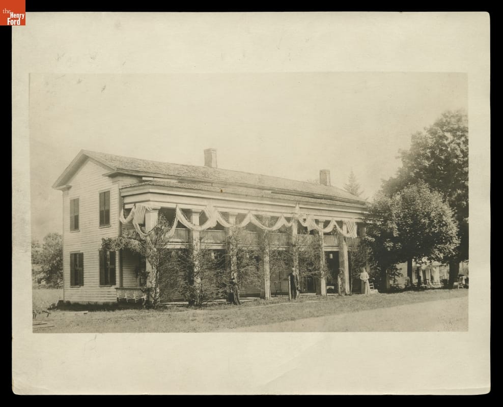 Black-and-white photo of long, two-story building with pillars in front of a first-story porch and second-story balcony