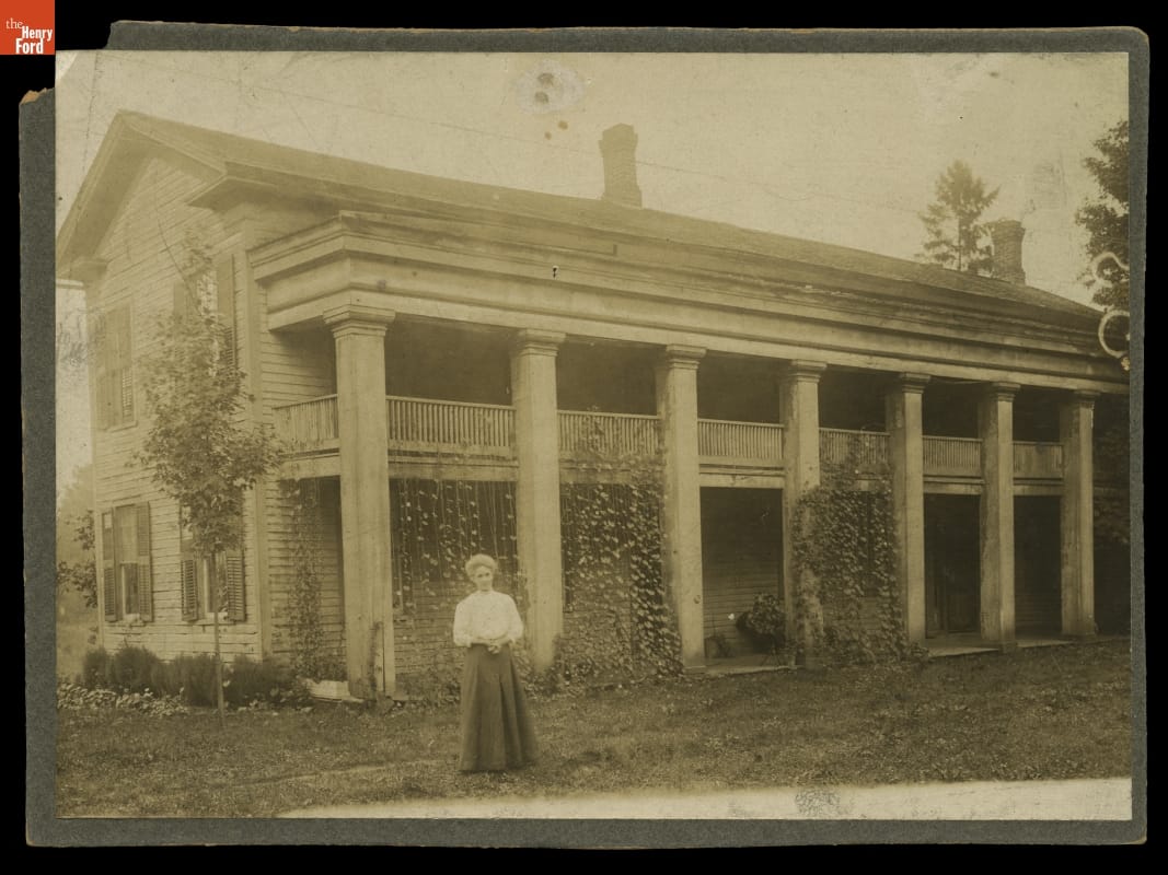 Eagle Tavern at Its Original Site, Clinton, Michigan, circa 1905 Woman stands in front of long, two-story building with columns