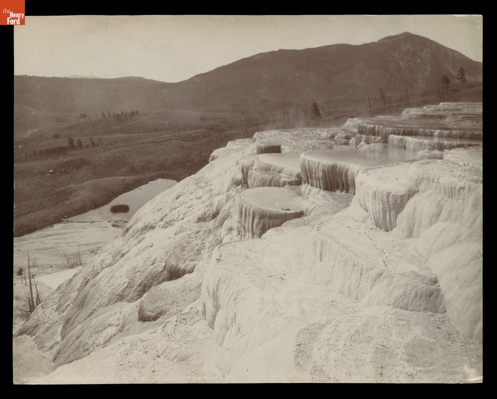 Black-and-white image of slope covered in water and/or calcified rock with hills or mountains in the background
