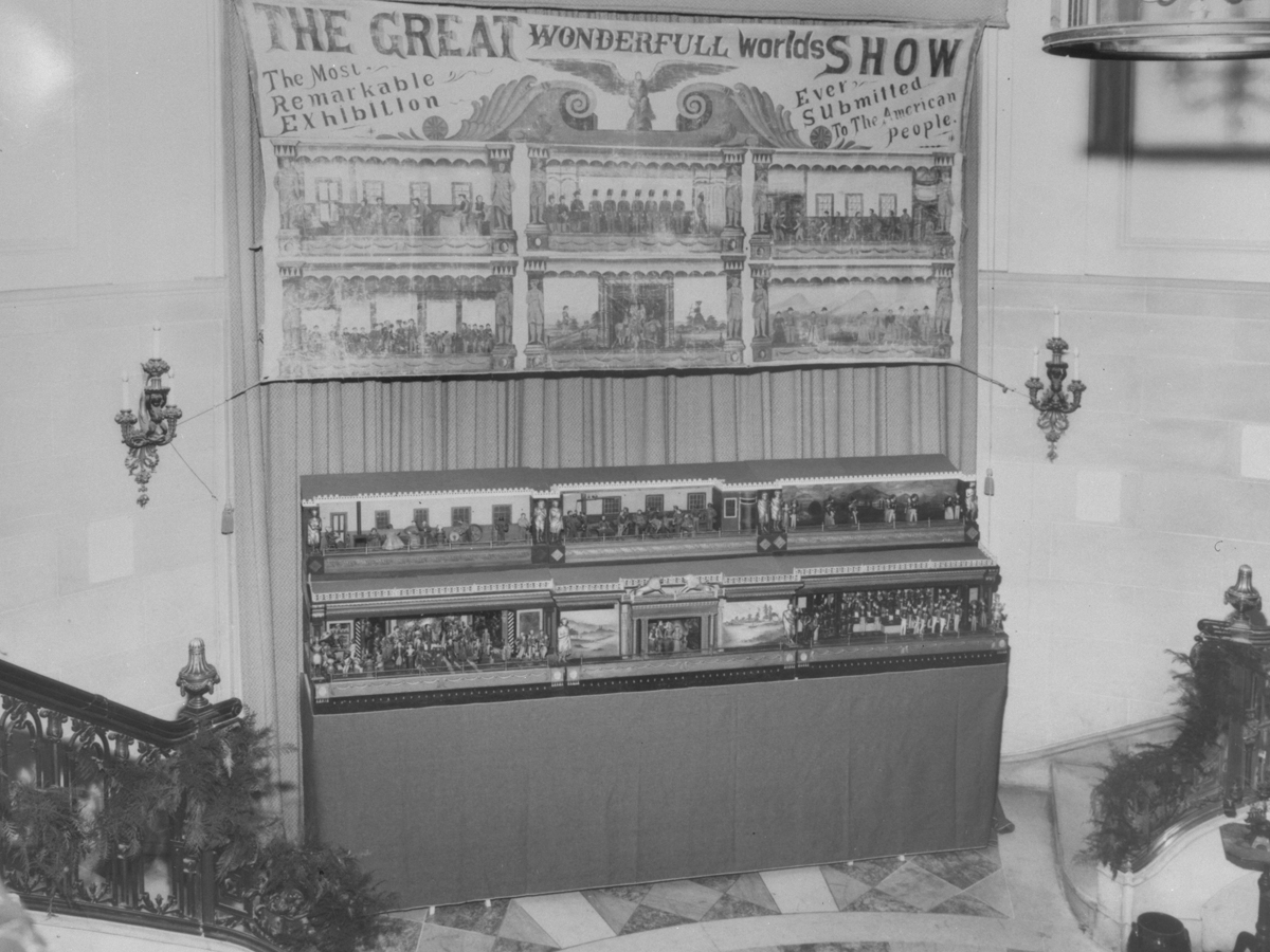 Exhibit with small wooden scenes on a platform underneath a banner