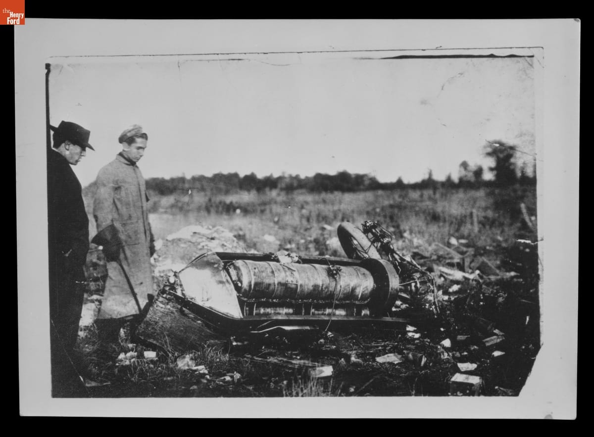 Wreckage of Ford Model K Black-and-white photo of two men staring at the crashed remains of a car in a field