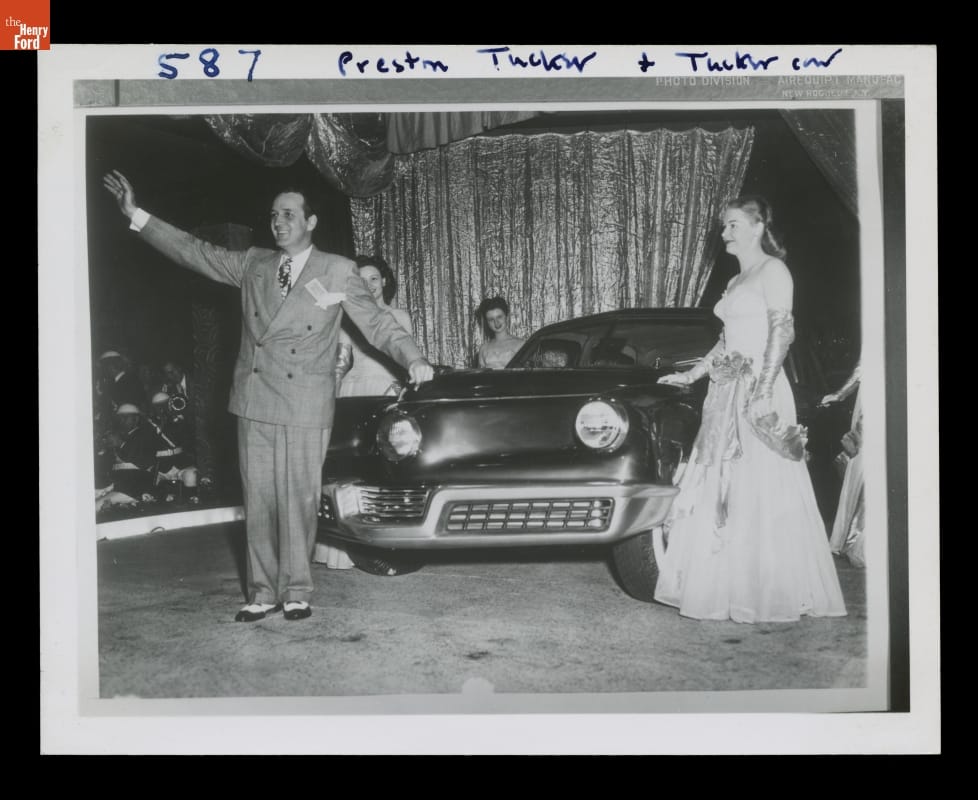 Preston Tucker Presenting the 1948 Tucker Sedan Black-and-white photo of man in suit and woman in fancy dress standing with two other women by a car in front of a curtain; man waves to crowd
