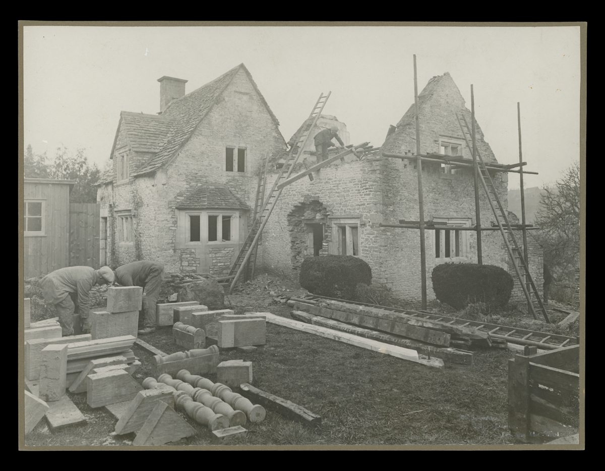 Partially disassembled stone building, with scaffolding around it and architectural elements laid out on the grass surrounding it