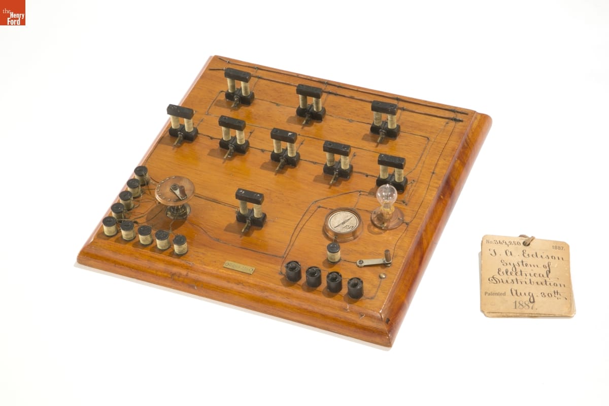 Wood board with small parts and wires attached to it; tag with handwritten text sits next to the board