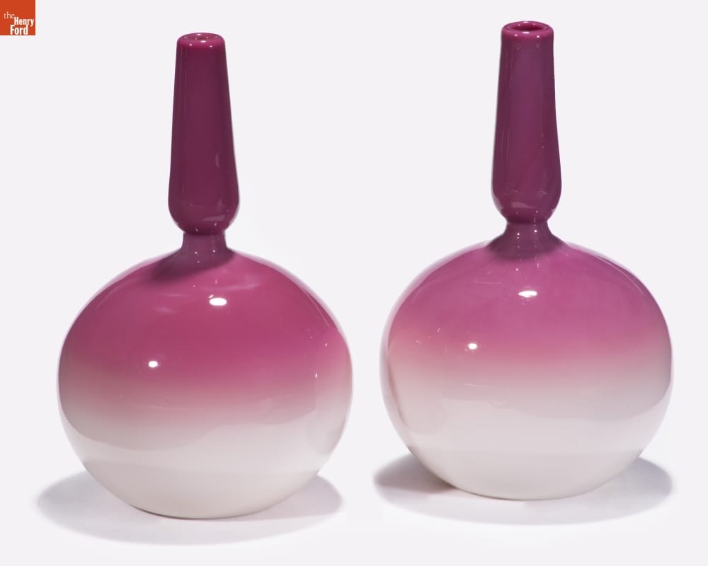 Two glass vases with rounded bodies and long, thin necks, morphing in color from white at the bottom to dark pink at the top