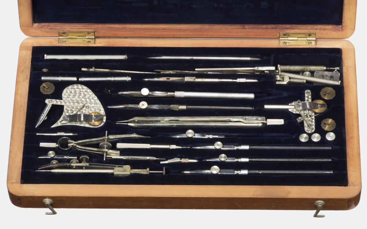 Wooden case open to reveal a number of silver drafting tools inside, set in black velvet