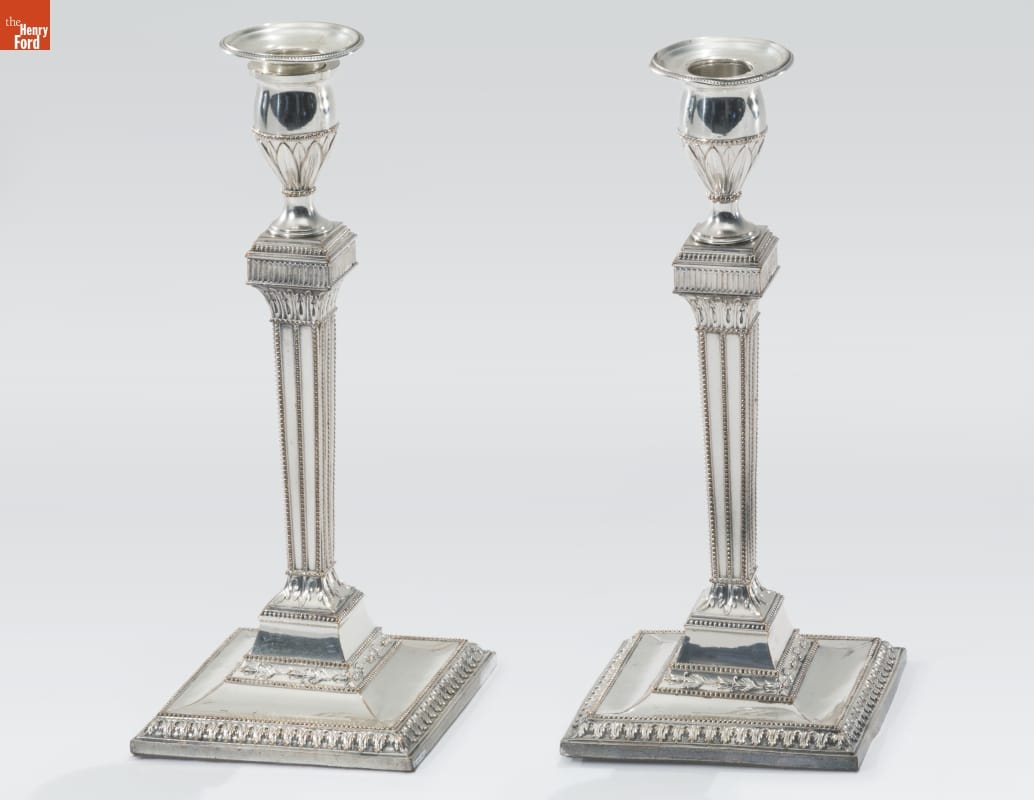 Tall thin silver candlesticks with broad square base, many decorative elements