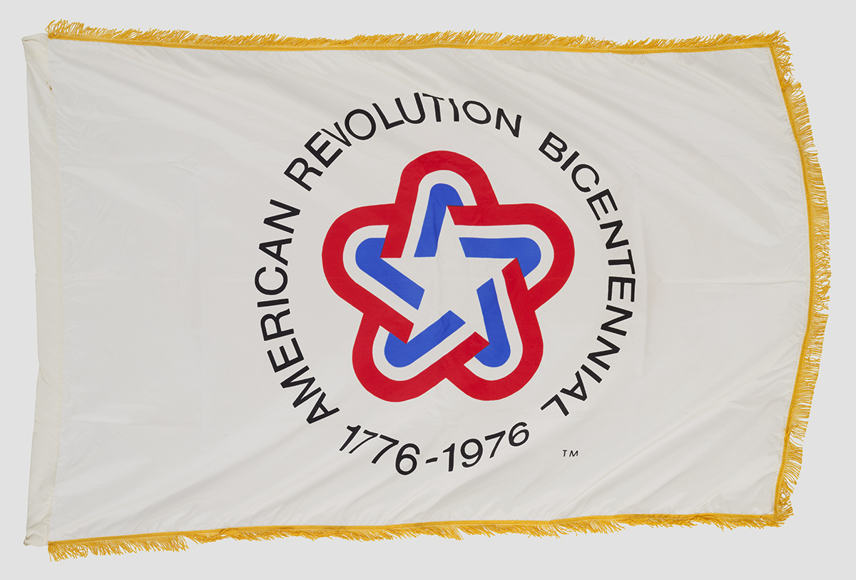 Gold-fringed white flag with rounded star in red, white, and blue and text 