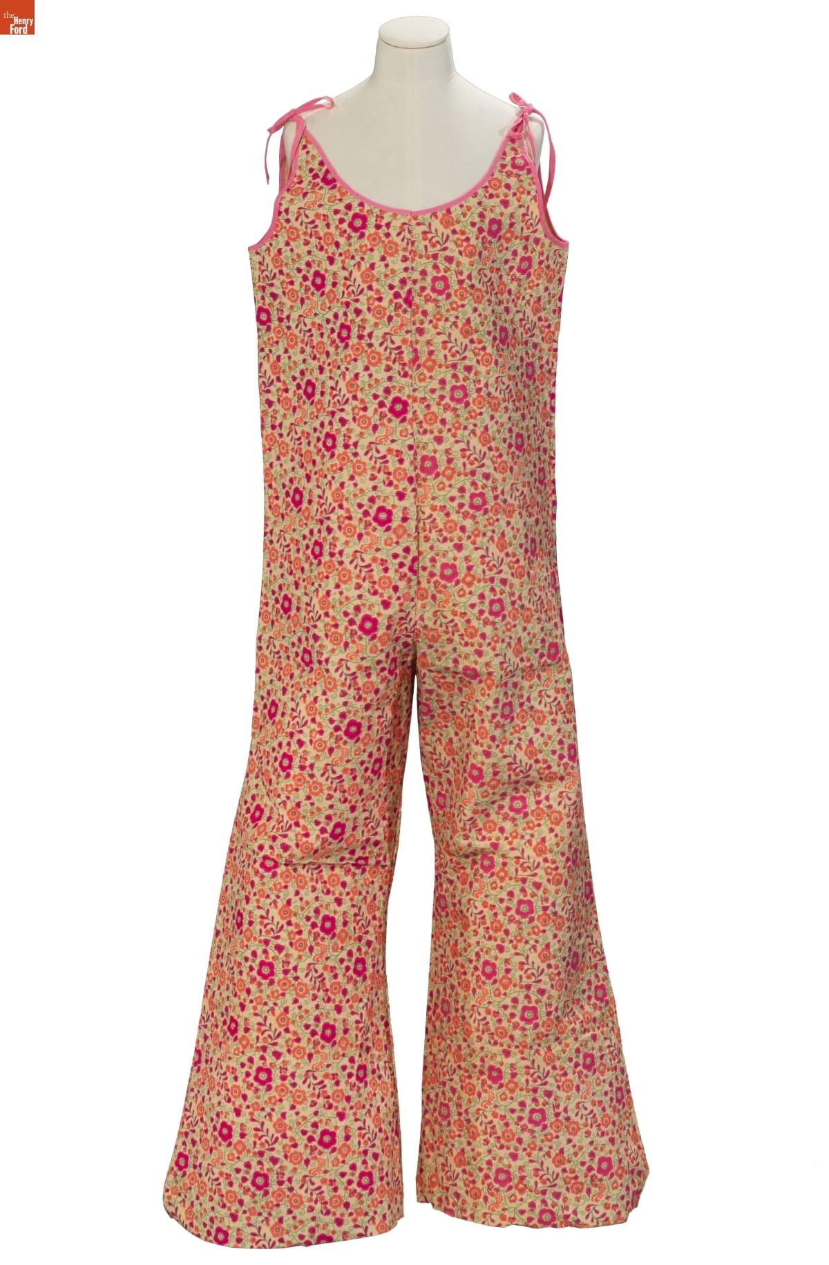 Sleeveless jumpsuit in green, red, and orange floral pattern with ties at the shoulders
