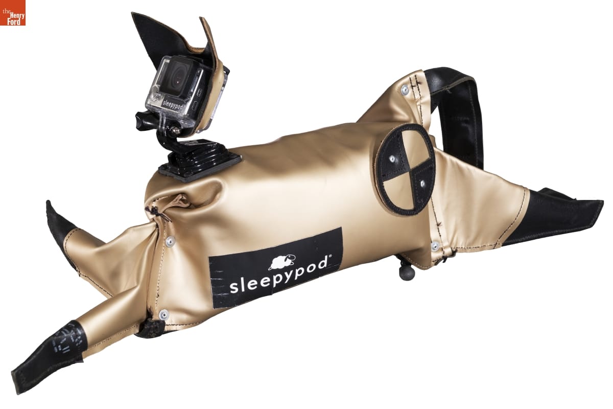 Champagne-colored fabric or plastic cat figure, with text and circular shape on side and camera where face would be
