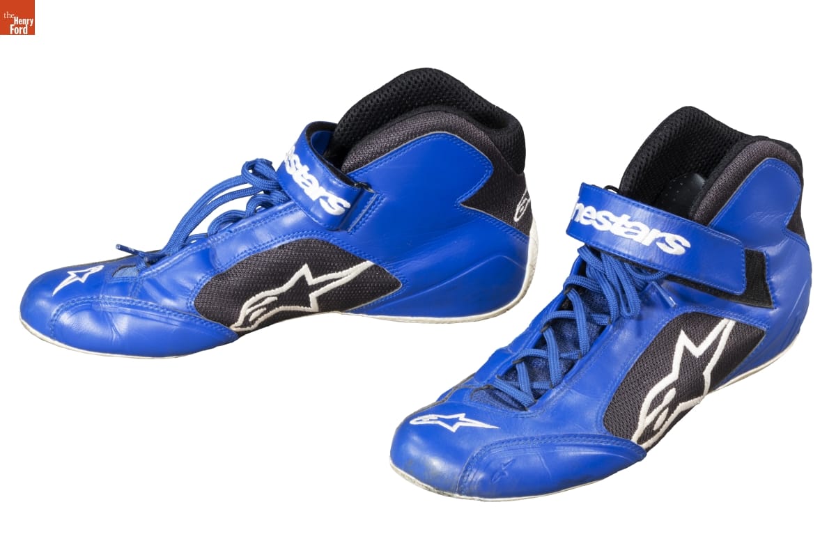 Blue sneakers with blue laces and a black patch containing an extended letter 