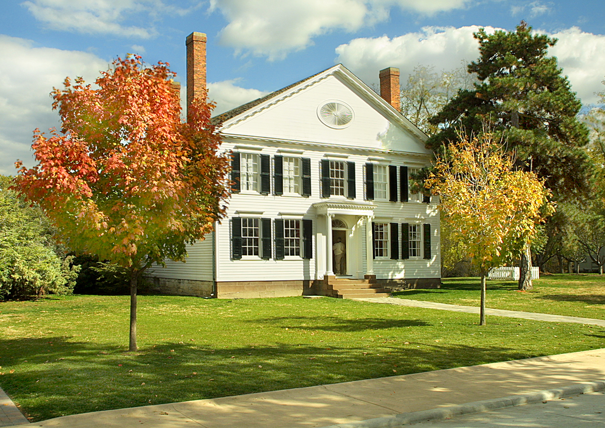 Two-story white wooden house on large grassy lawn with many trees around it