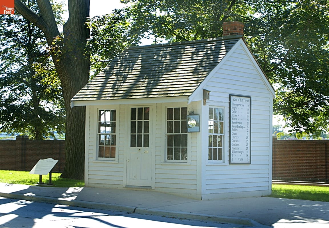Small white wooden building with sign on side, shaded by a tree