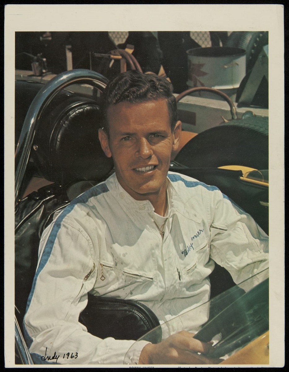 Young man wearing jumpsuit looks at camera as he sits in open race car cockpit