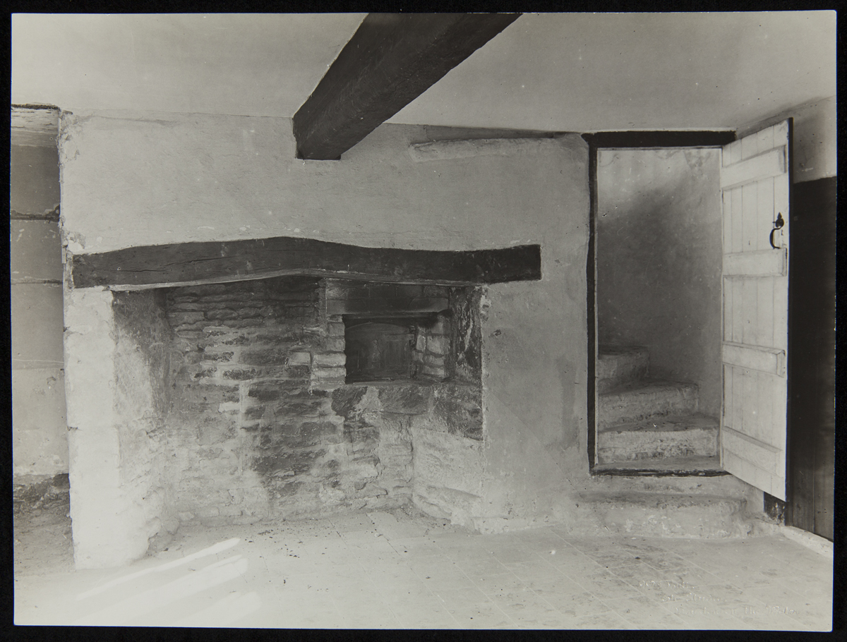 Bare interior of room with low ceiling, large fireplace, and door open to reveal spiral staircase leading upwards
