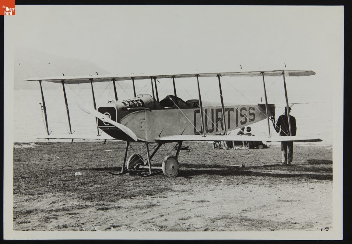Curtiss JN Man standing at back of airplane with large text
