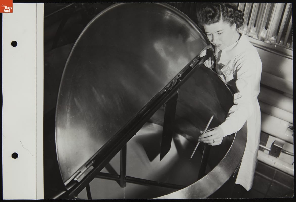 Mrs. Hardy Checking Soybean Milk in Ford Lab, March 1944 Woman holds stick or gauge over large metal vat containing liquid