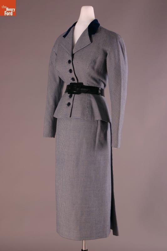 Long gray skirt and gray jacket with black belt, buttons, and collar