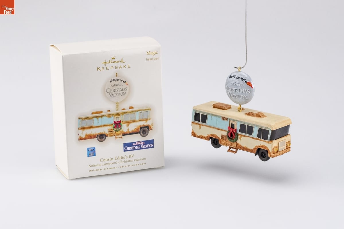 Ornament of rusted beige RV with wreath on door, dangling from round silver button reading 
