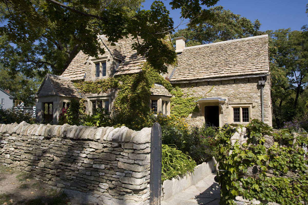 Stone house with ivy growing on it, behind stone wall and garden