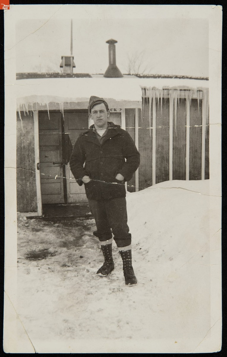 Man Standing outside a Civilian Conservation Corps Barracks in Winter, circa 1935 Man in coat and boots stands in snow outside simple structure covered in snow with icicles handing from eaves