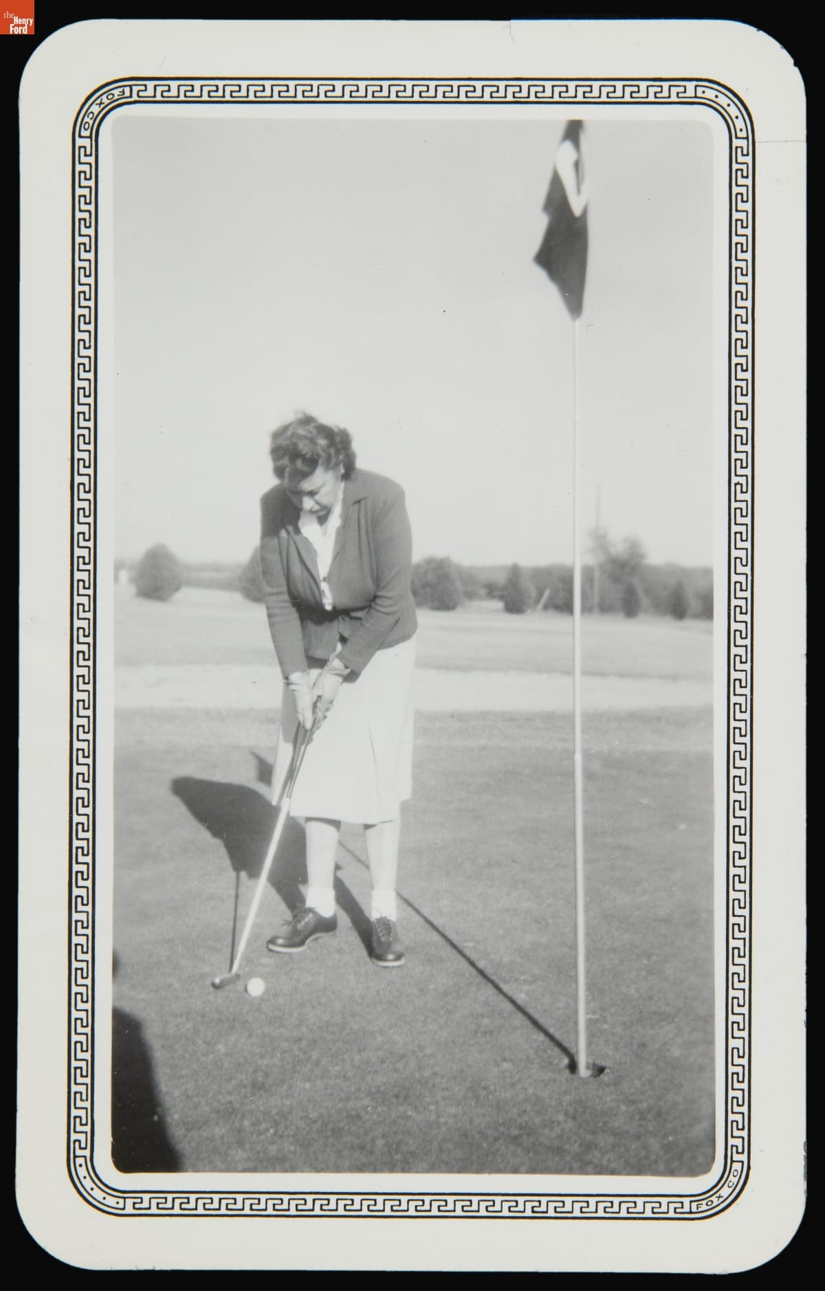 Woman in skirt and jacket bends over to putt a golf ball with hole marked with flag nearby