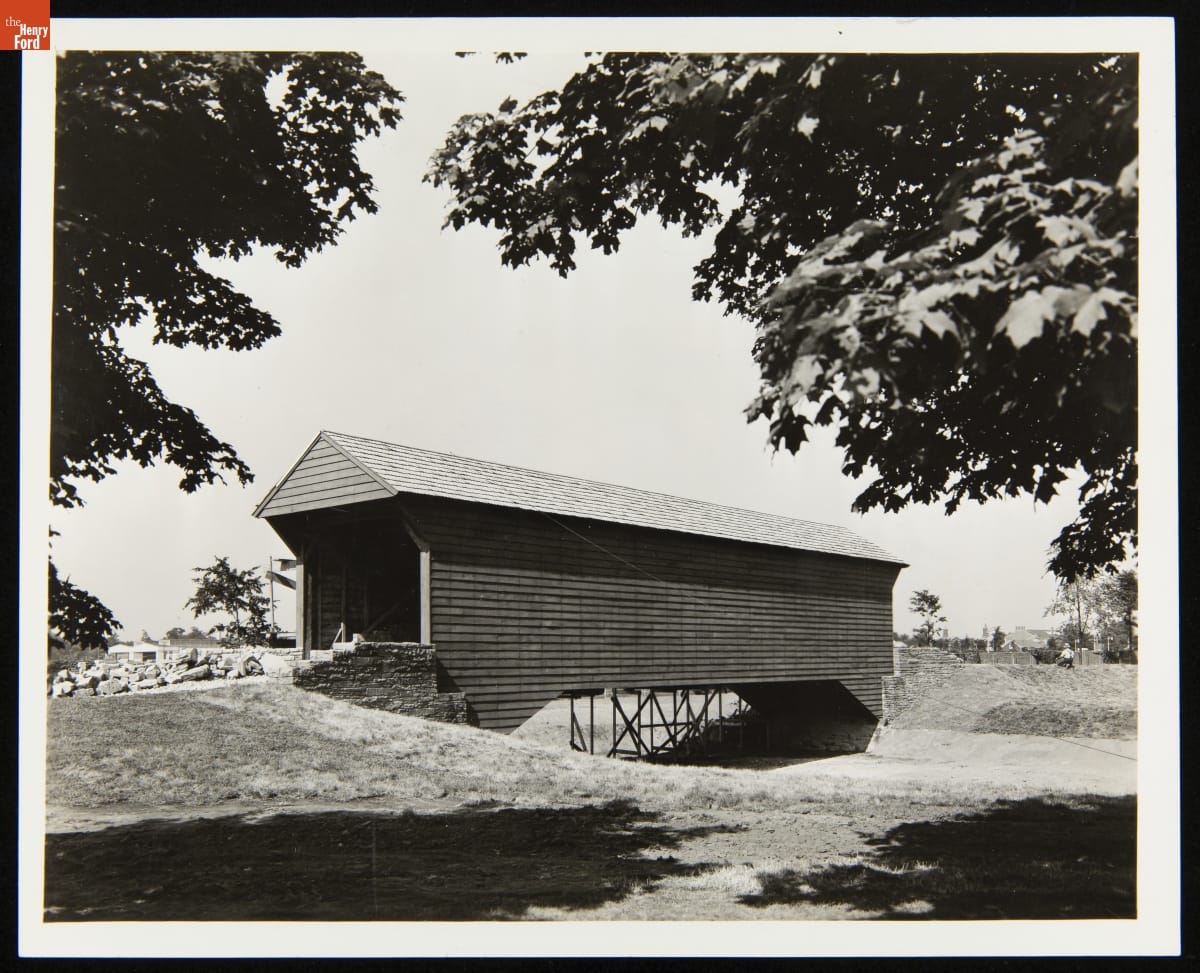 Black-and-white photo of wooden covered bridge over dry streambed