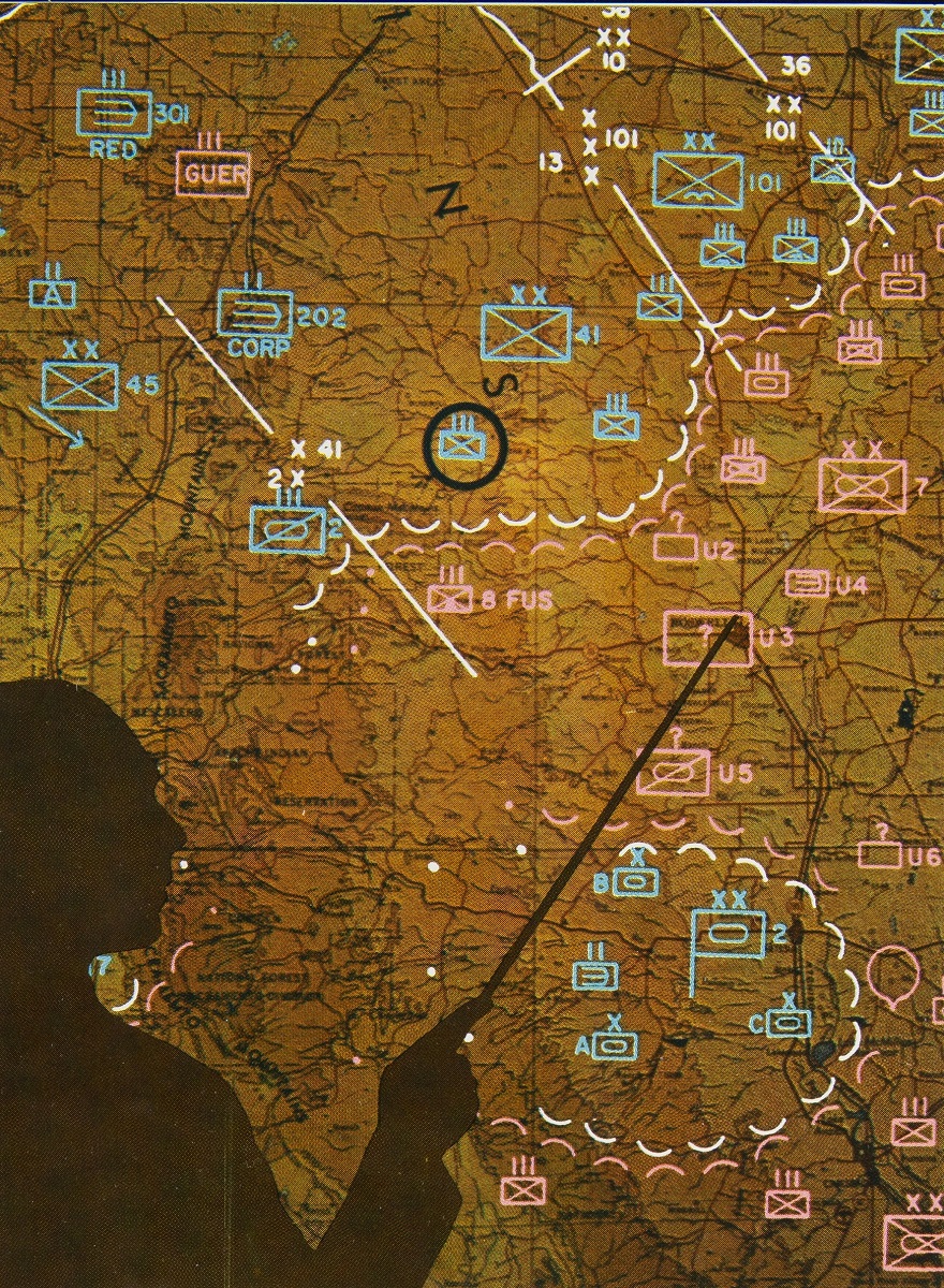 Silhouette of person holding pointer to topographic map with pink, blue, and white projected notations on it 