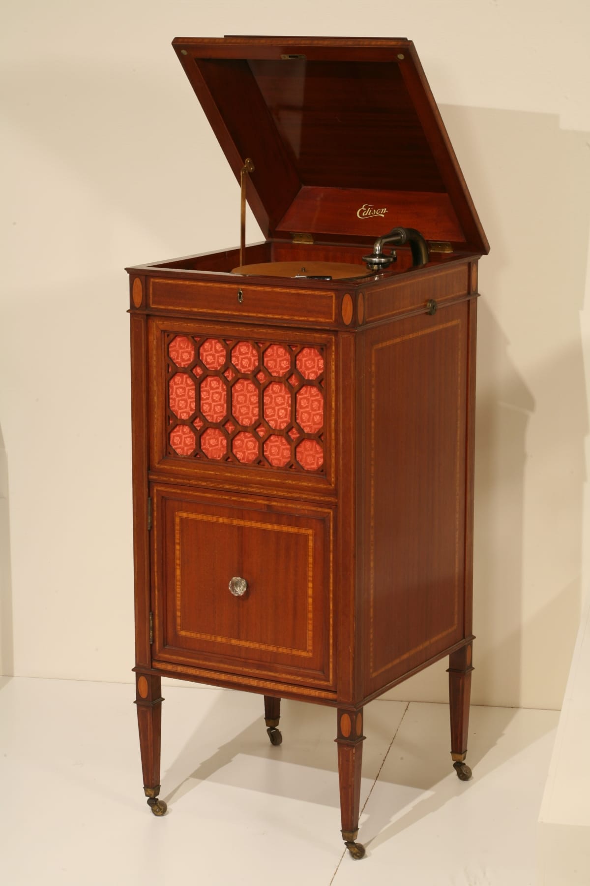 Wooden cabinet with four thin legs and decorative elements; top open to show machinery