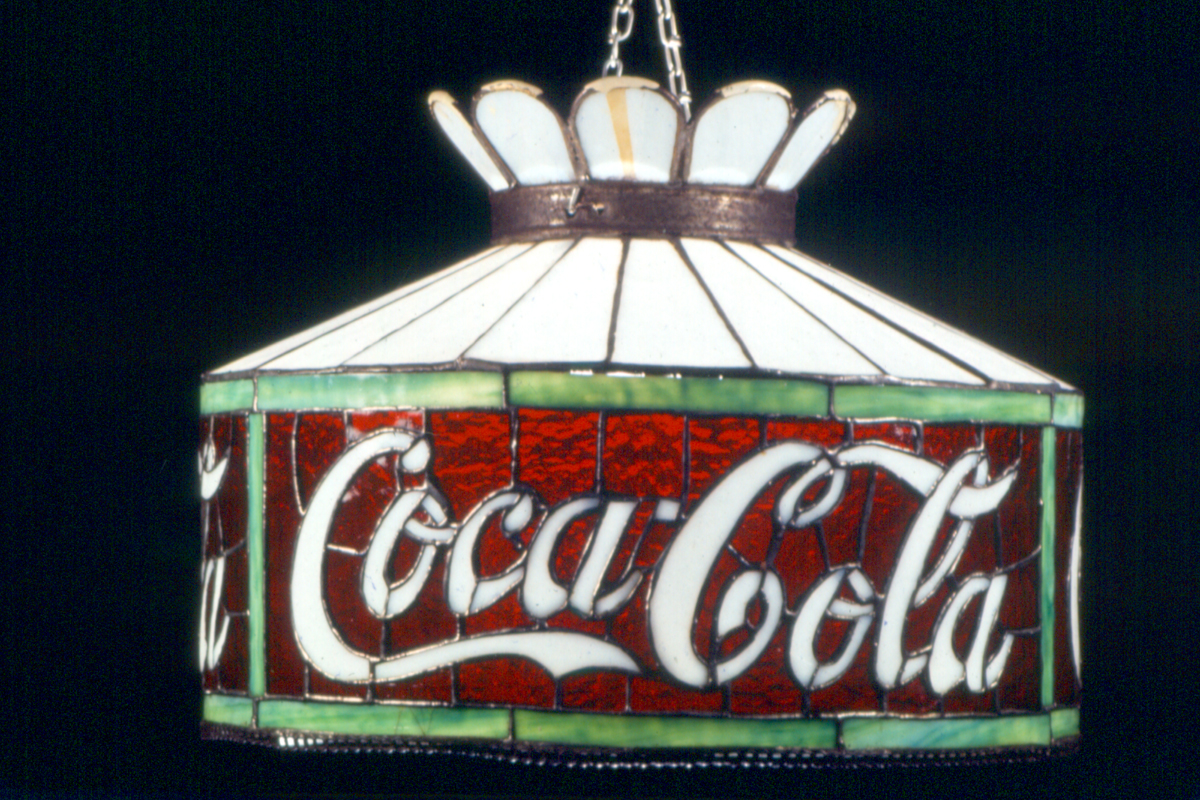 Stained glass lamp in shades of white, green, and red, with white cursive text 