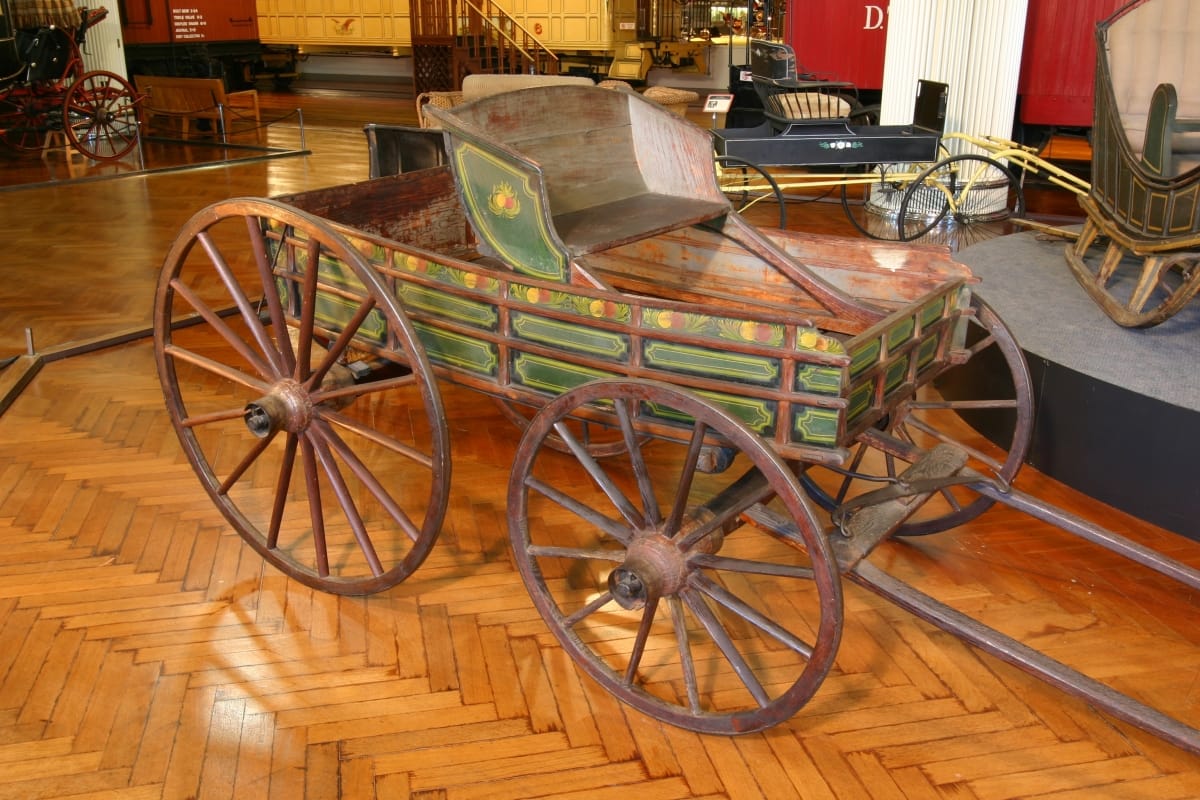 Open woden wagon painted with decorative pattern in green and other colors, with two large rear wheels and two smaller front wheels