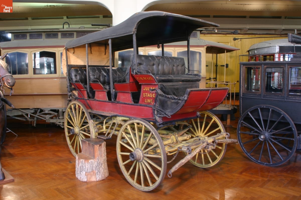 Red wagon with black cover, open sides, and several rows of seating; also has text on side