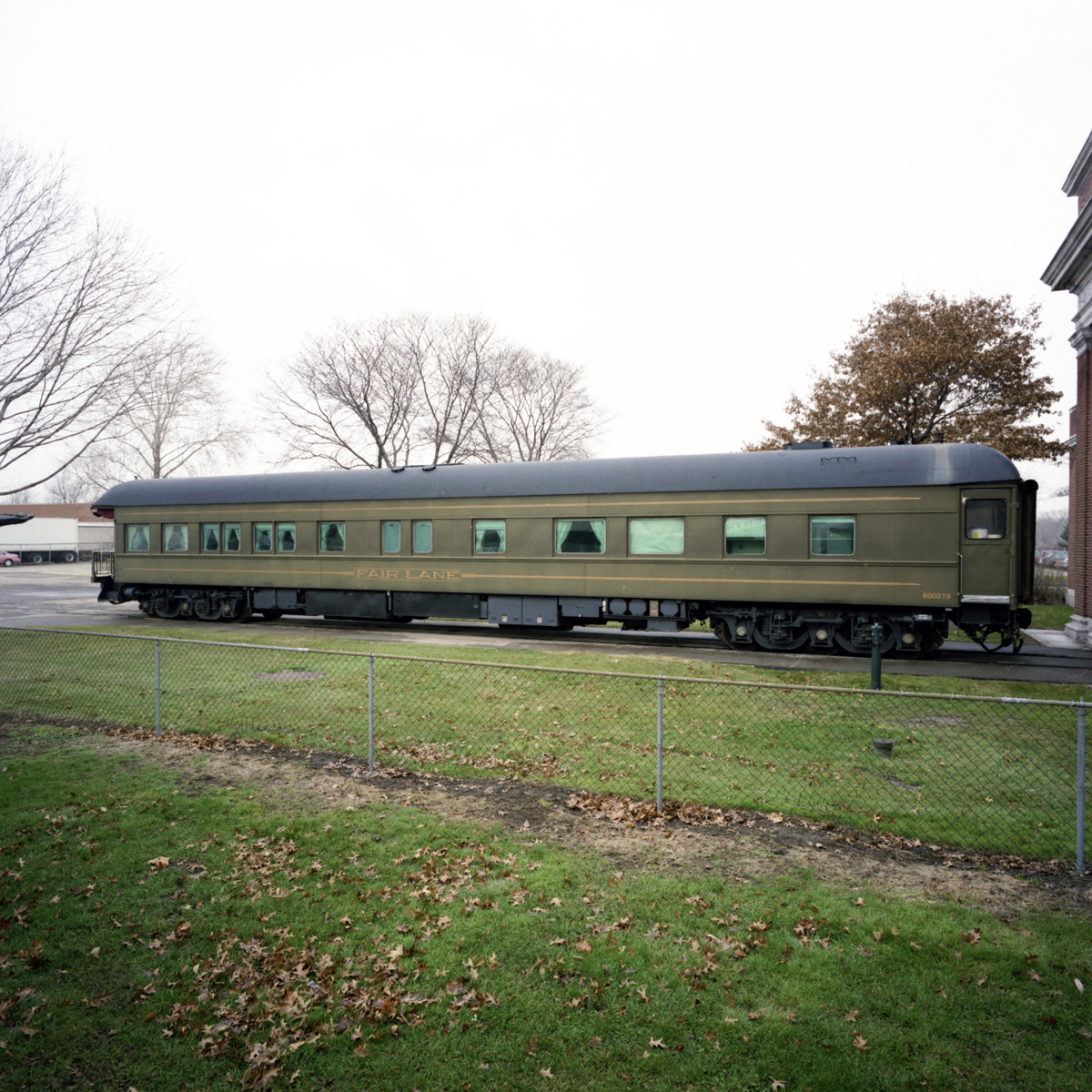 Long, army-green rail car on tracks in a field