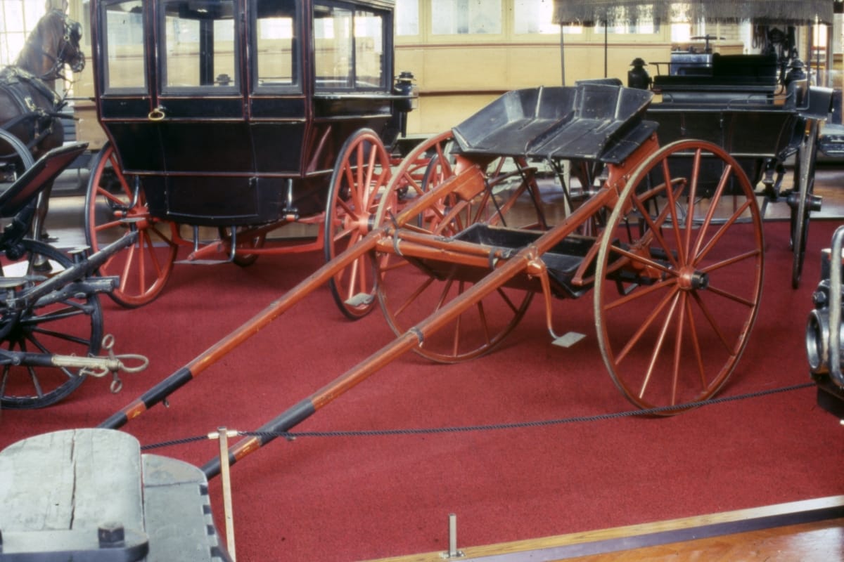 Simple open cart with two large wheels, in a room with other carriages