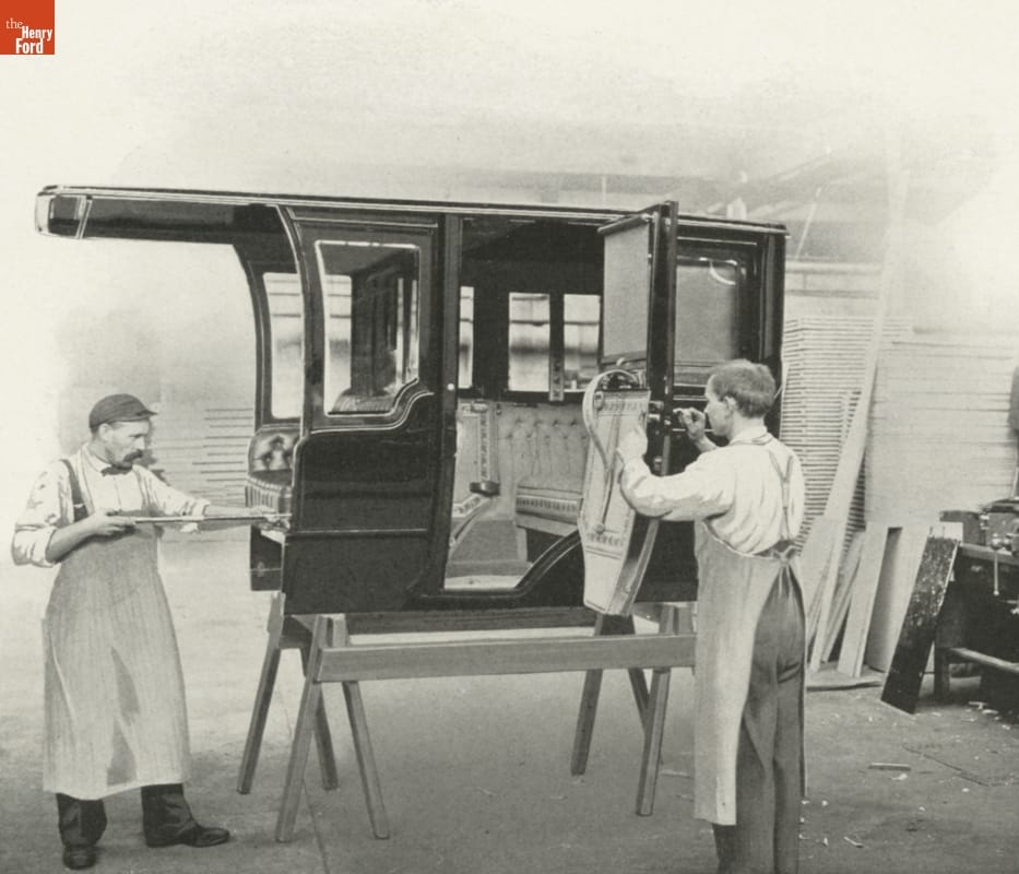 Two men work on a car body on sawhorses