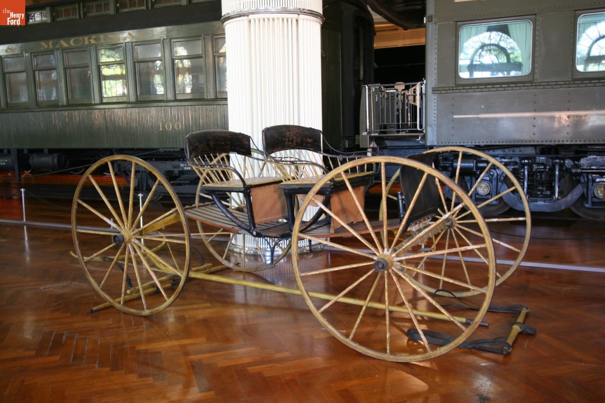 Minimal wooden transport with two seats atop a wooden platform with four large wheels