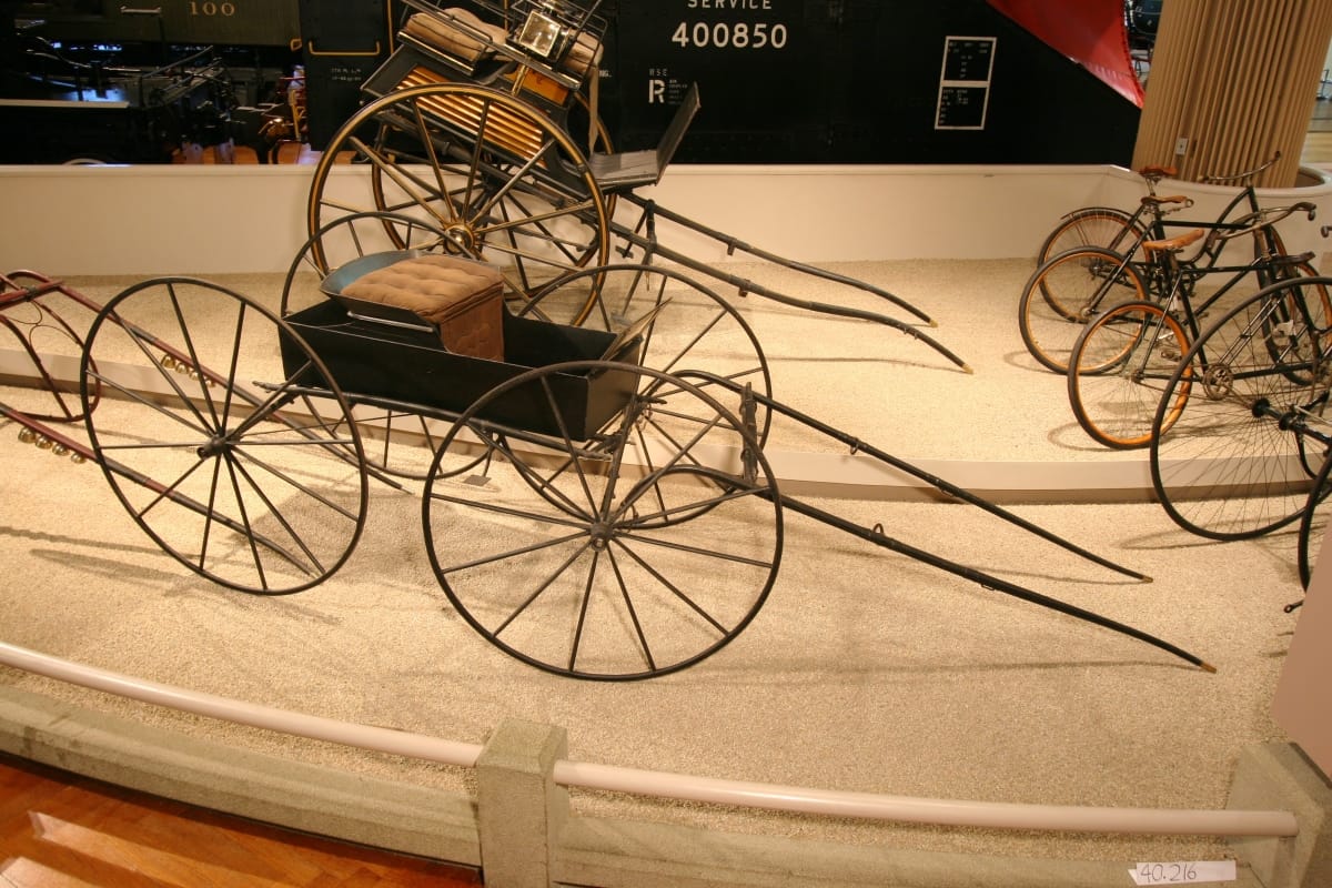 Minimal carriage with low tray-like structure containing padded seat atop four large wheels