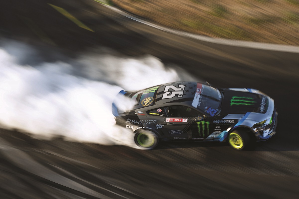 Aerial shot of gray race car with text and logos turning on racetrack and trailing smoke