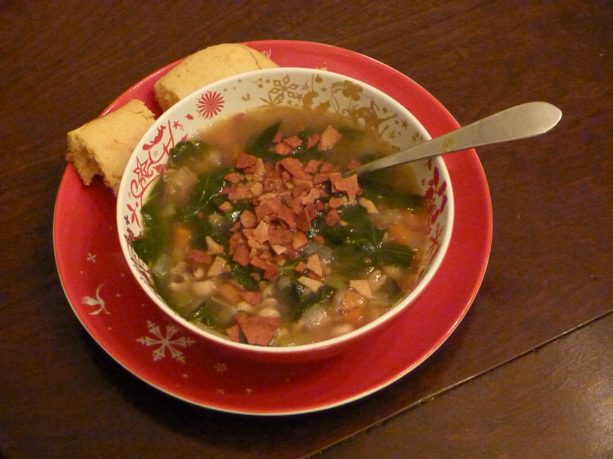Bowl filled with soup and topped with vegetarian bacon; cornbread on side