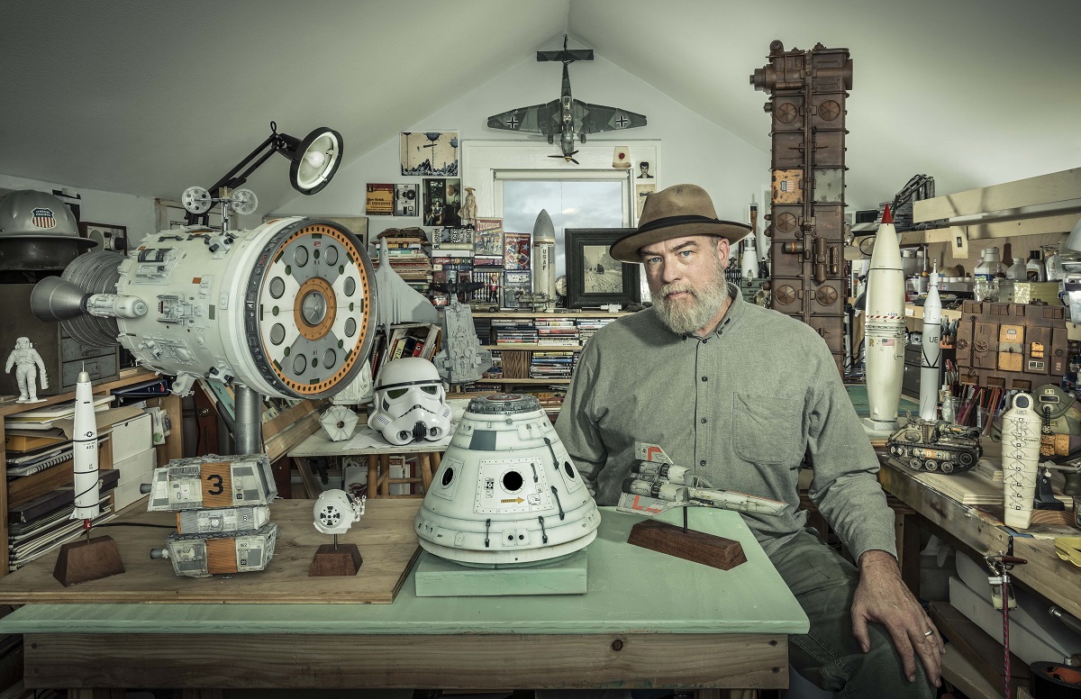 Dan Winters Man in fedora sits in a workshop crowded with models (mostly space-related), books, and other items